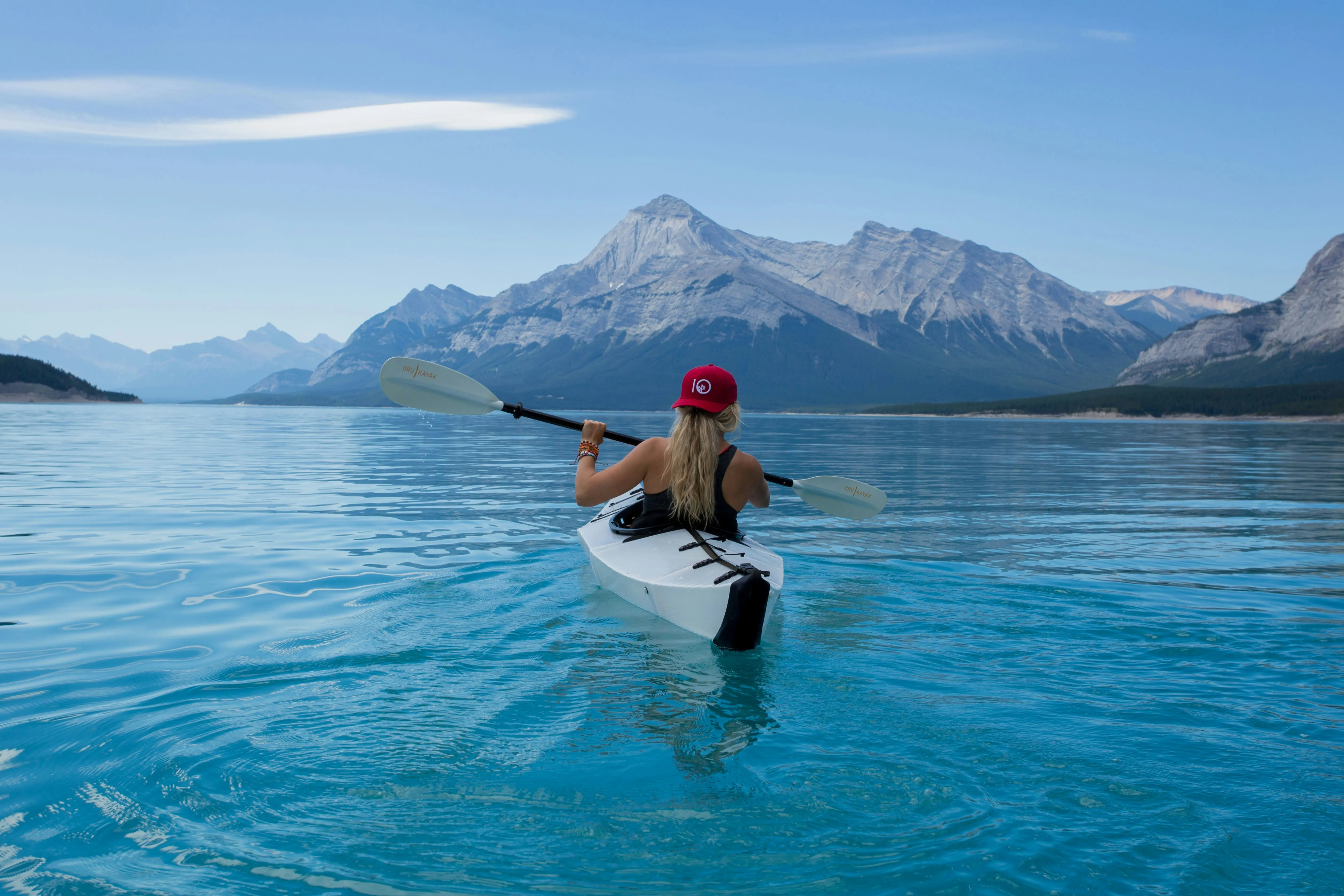 Woman kayaking away with mountains in the background